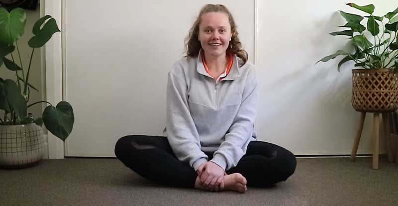Gym Instructor Kim sitting on her carpet at home with legs crossed and smiling