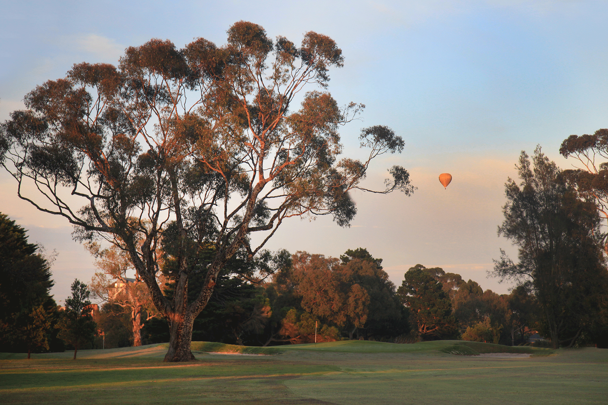 The golf course at sunrise with a hot air balloon in the distance