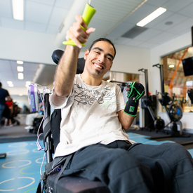 A man with disability in Empower+ program at Richmond sitting in a wheelchair and smiling in the gym