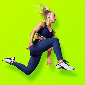 A blonde girl jumping in the air in activewear with a yellow background
