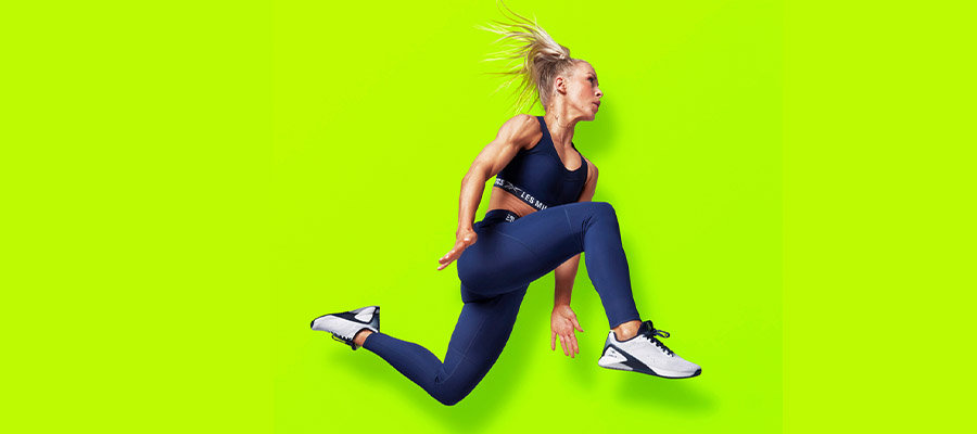 A blonde girl jumping in the air in activewear with a yellow background