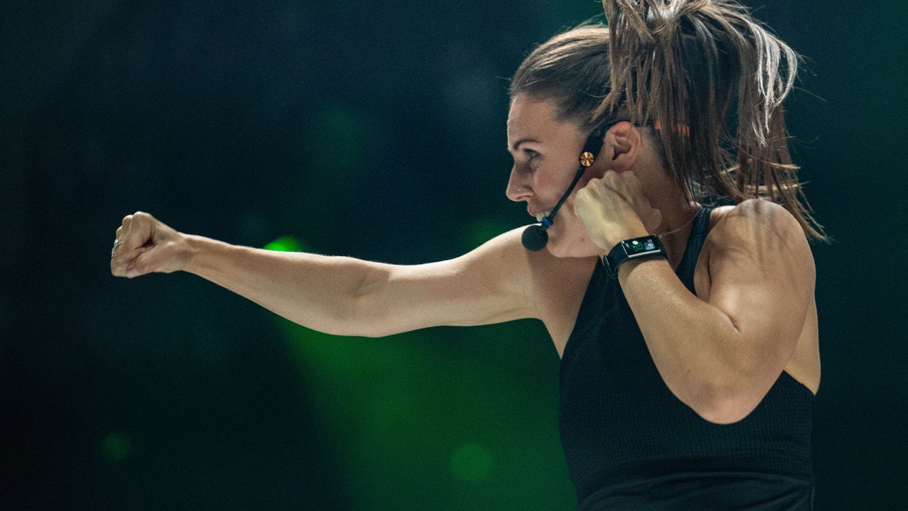 A female Body Combat instructor doing a boxing motion wearing a headset microphone