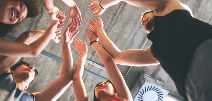 A group of people in a group exercise class putting their hands into the centre and smiling