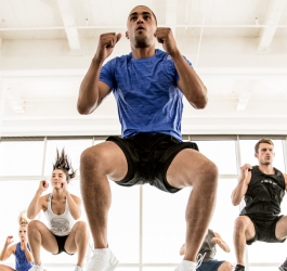 A group of men and women doing a squat jump in a group exercise class