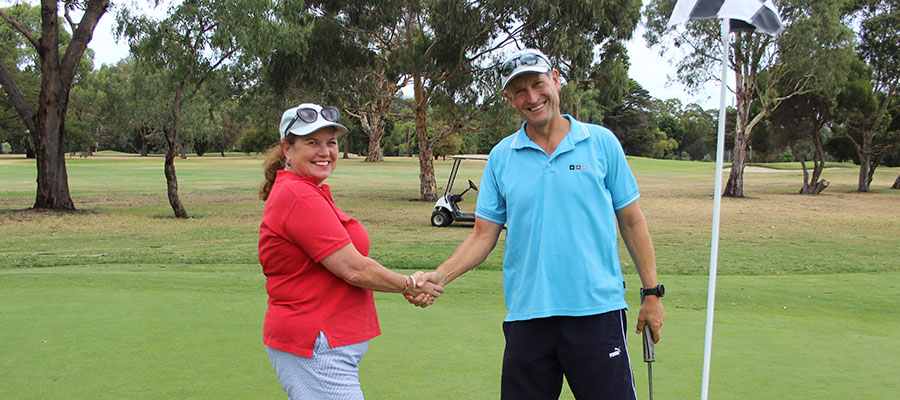 A woman and man shaking hands on a golf course green