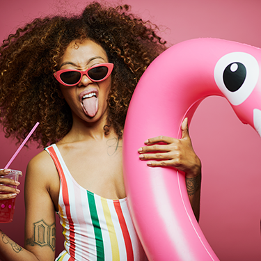 Woman with a swan blow up pool toy, a drink and pink sunnies smiling