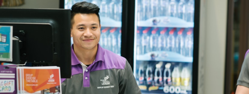 A young man at the customer service desk at a Yarra Leisure facility smiling towards a customer