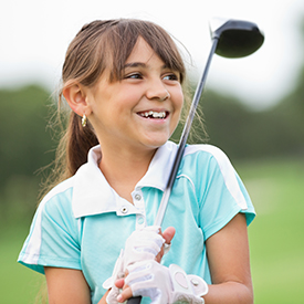 Young girl smiling and holding a golf club over her shoulder