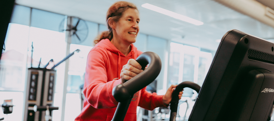 A woman in a red jumper on a cross trainer at Richmond Recreation Centre and smiling