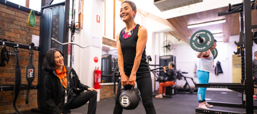 A woman lifting a kettlebell in the Collingwood Estate Gym with a Gym Instructor watching and smiling