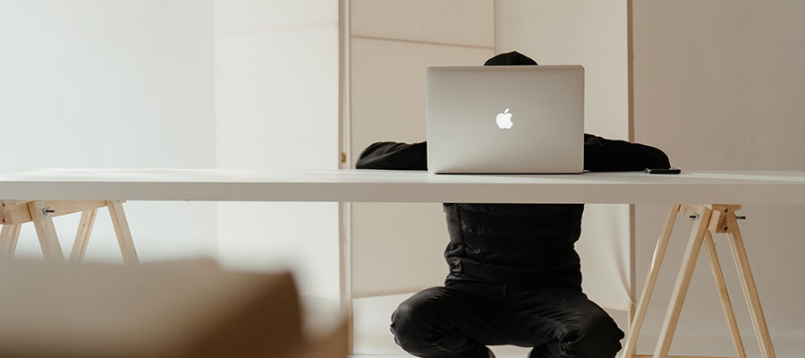 A man on a macbook computer sitting at a table with his head behind the screen barely visible