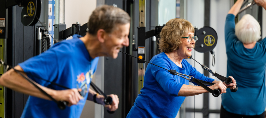 Older adults working out on dual pulley cable machine.