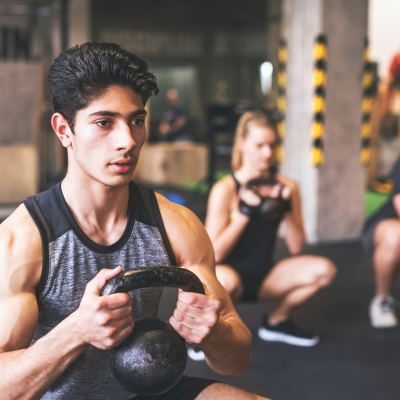 Young man with training partners lifting kettlebell in gym.