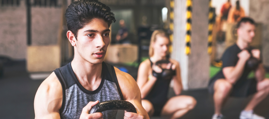 Young man with training partners lifting kettlebell in gym.