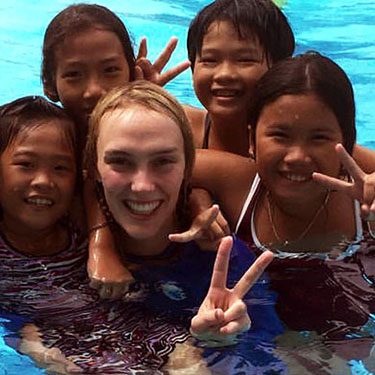 A swimming instructor in the pool smiling to camera with children in the class