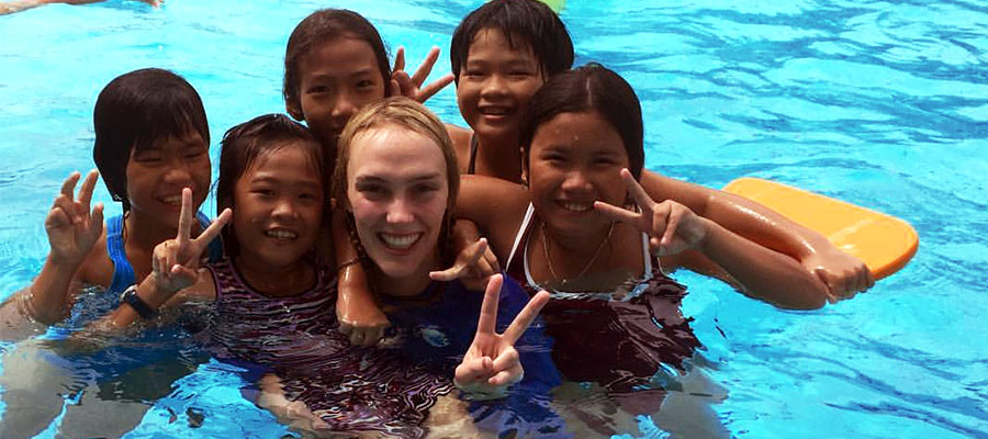 A swimming instructor in the pool smiling to camera with children in the class
