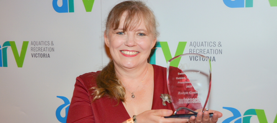 Robyn holding her award infront of the ARV photo wall and smiling holding her trophy