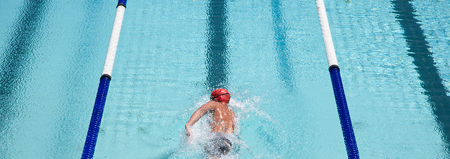 A man swimming freestyle in a lane of a pool wearing a red cap