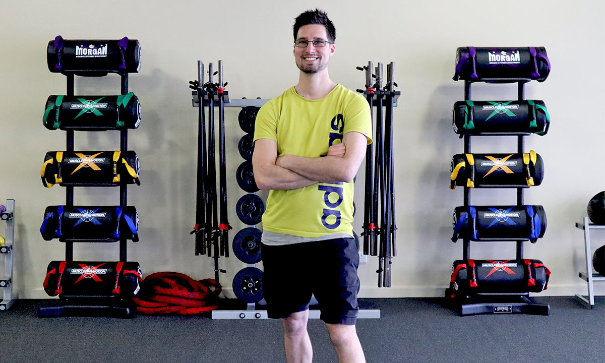 Gym Instructor Adam standing with his arms crossed in a yellow shit and smiling