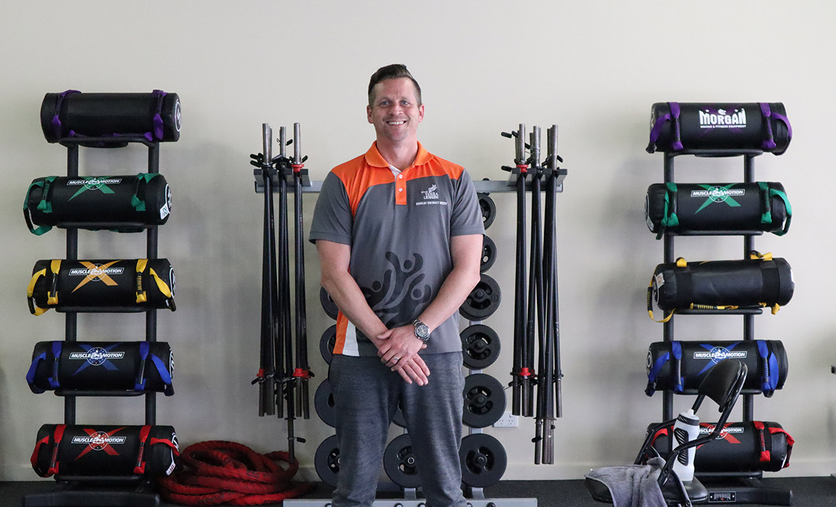 Gym Instructor Andrew crossing his hands and smiling standing in the gym