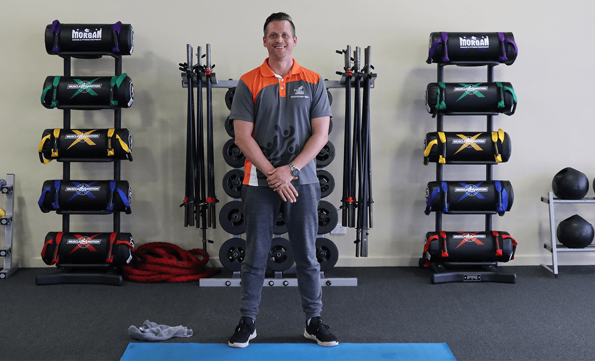 Gym Instructor Andrew standing in the group exercise room with his arms down smiling