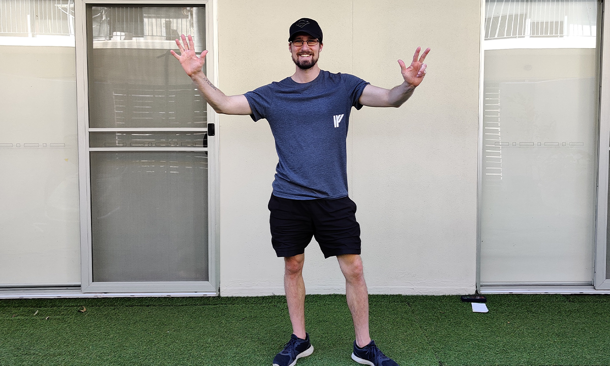 Gym Instructor Adam standing in his backyard with his hands in the air and smiling