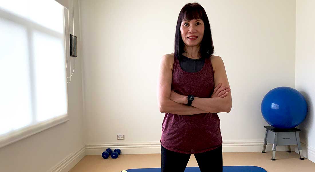 Gym Instructor Sharon in her active wear and arms crossed smiling in her home gym
