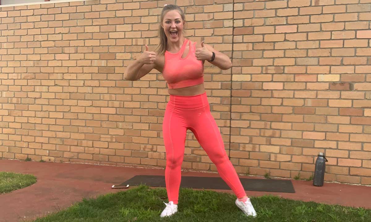Gym Instructor Mel in pink active wear standing on the grass at her home smiling with thumbs up