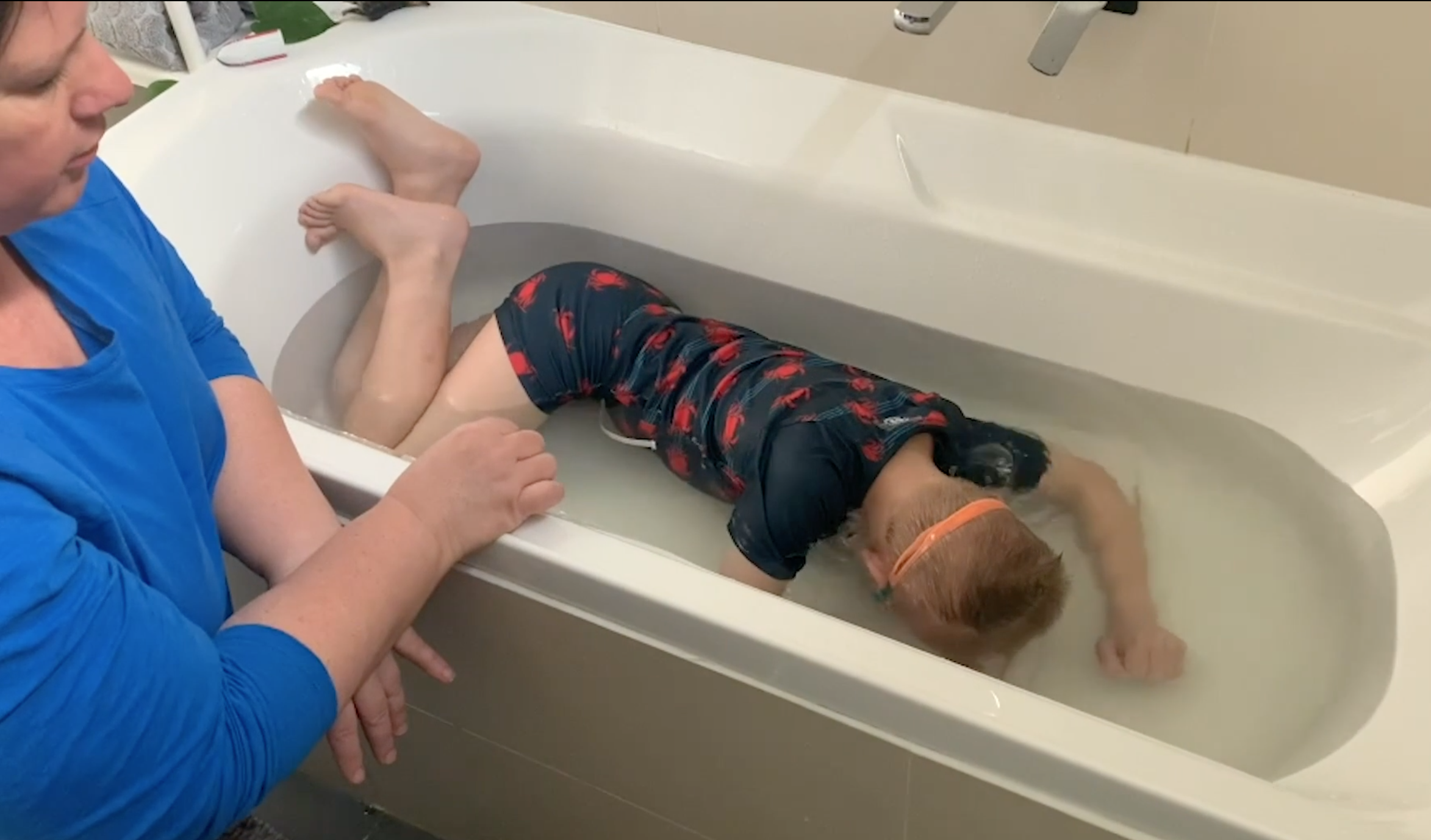 Yarra Leisure swim instructor Anna practicing putting eyes and ears underwater in a bath with her young son in the bath at home