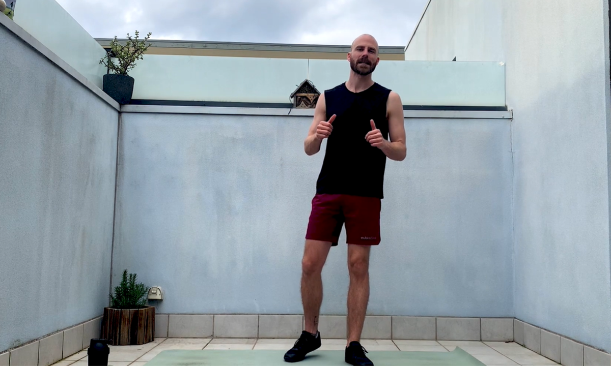Yarra Leisure instructor Leigh standing on a mat on a balcony at home with his thumbs up and smiling