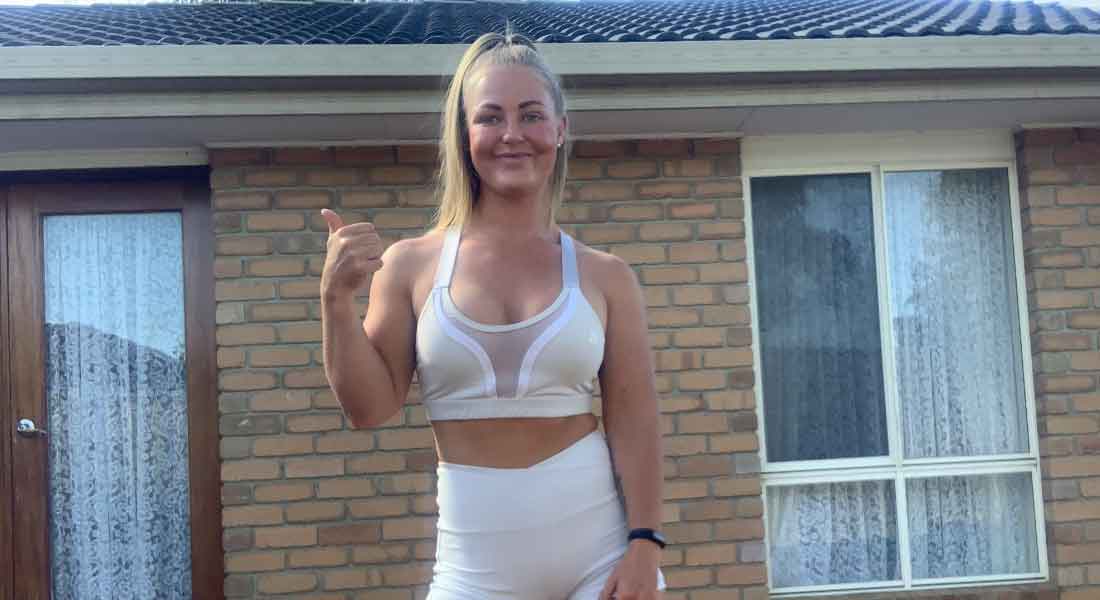 Gym Instructor Mel standing in her white active wear and smiling with her thumbs up