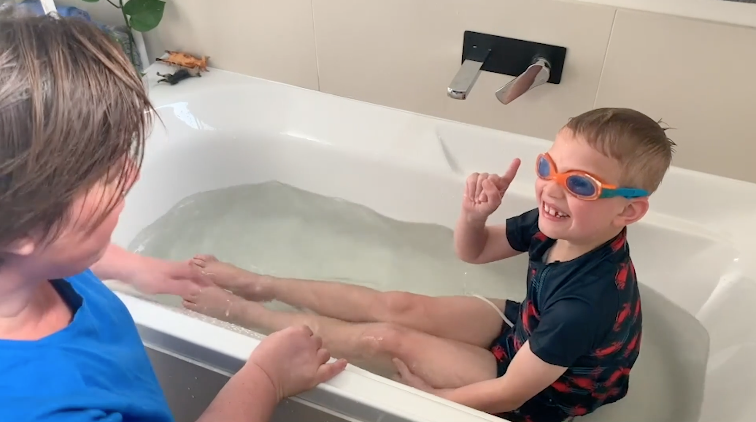 Swimming instructor Anna teaching a young boy how to kick in a bath