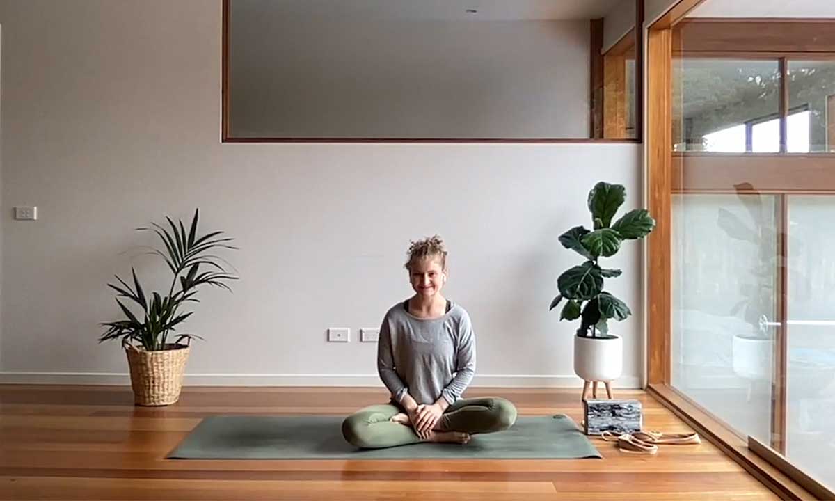 Yoga instructor Caragh sitting on a yoga mat at home smiling