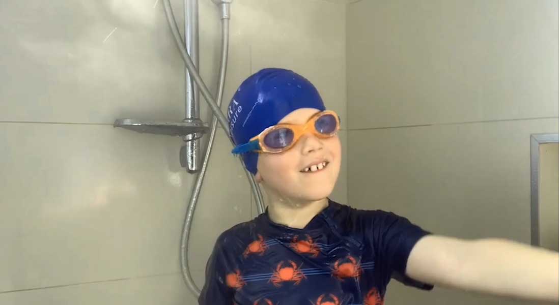 Swim Instructor Anna's son in the shower with a swimming cap, goggles and bathers in and smiling