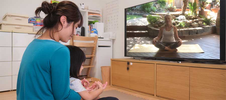 A woman and her child sitting in front of their television doing yoga at home