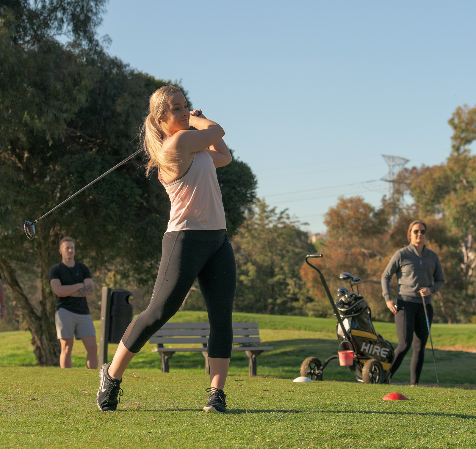 Image of female golfer swinging her club at Burnley Golf Course, with three other people in the background.