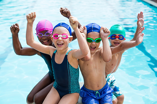 Young children sitting on the edge of the pool with their hands up smiling